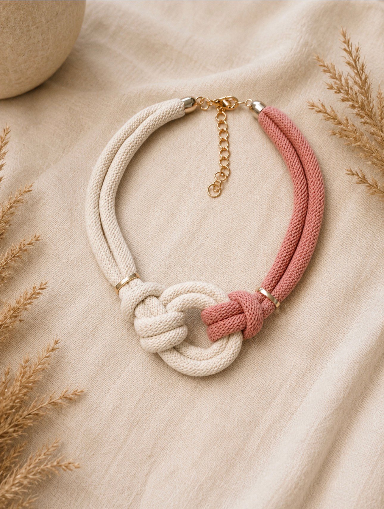 Collier textile naturel et rose poudré, noué sur une étoffe beige